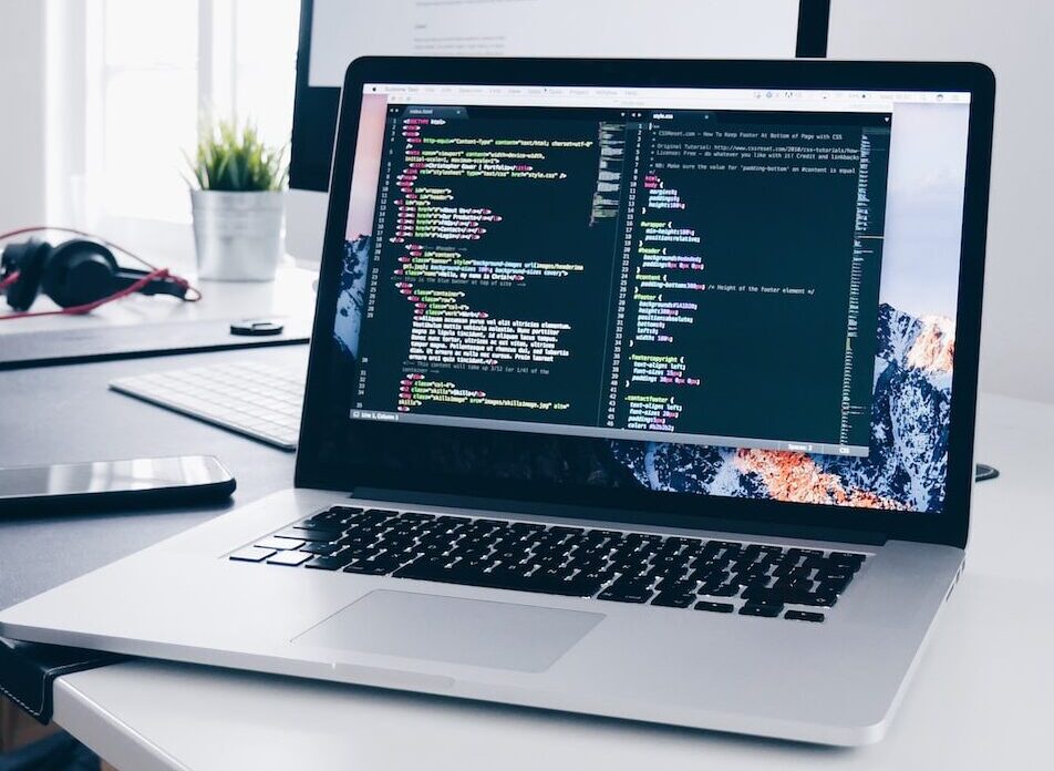 A MacBook with lines of code on its screen on a busy desk